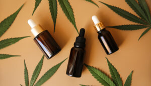 Glass bottles with CBD oil, THC tincture and hemp leaves on a marble background.